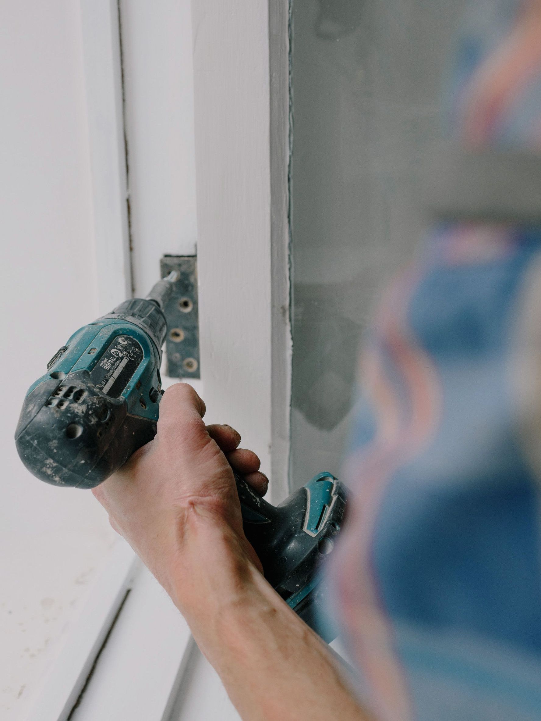 Crop bearded guy installing new wooden window with contemporary screwdriver and metal hinge during renovation process in apartment